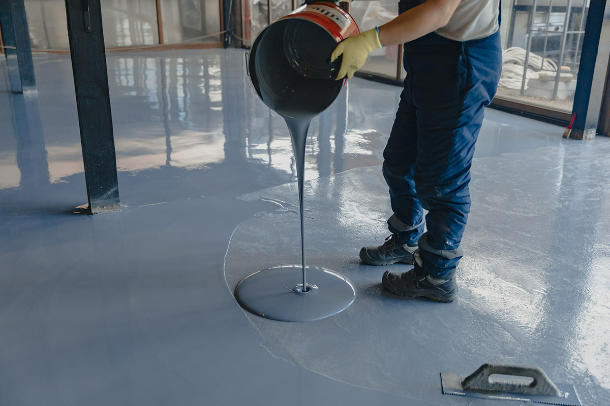 A worker is laying an epoxy floor in a warehouse