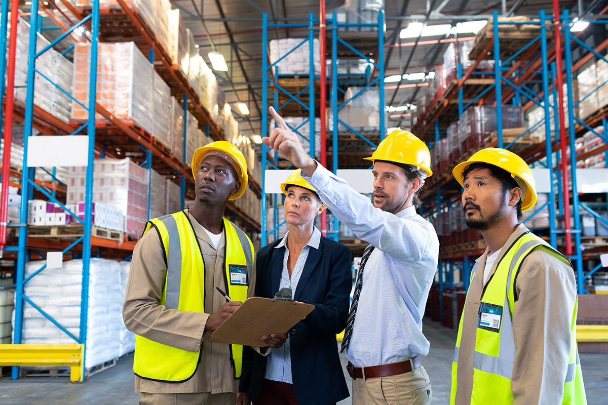 A man points to something in a warehouse - he is with a group of colleagues